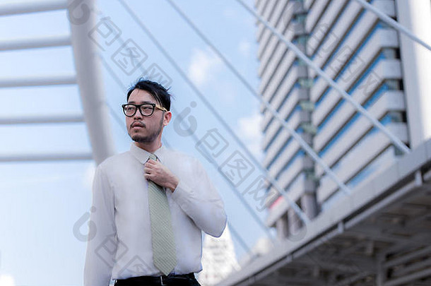 英俊的亚洲商人穿着正装站着的肖像。城市环境中的城市背景