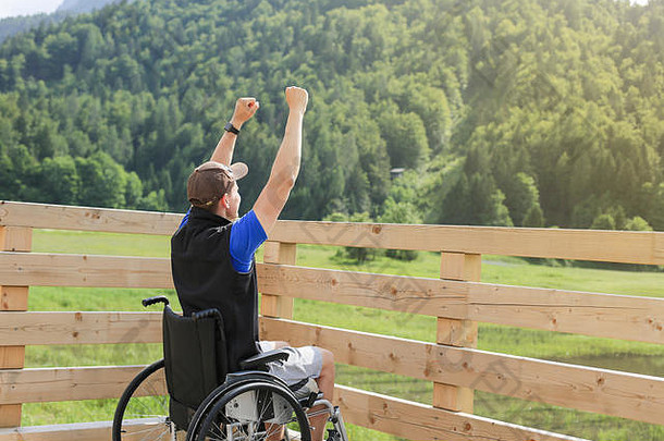 一个坐在轮椅上的残疾年轻人在大自然中感到兴奋和充满乐观，就像一个胜利者