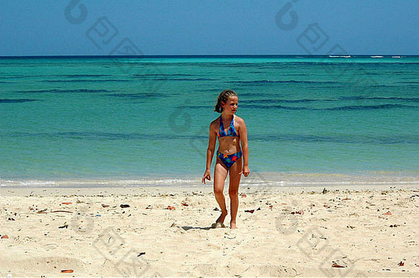 穿着比基尼在热带海滩上散步的年轻女孩
