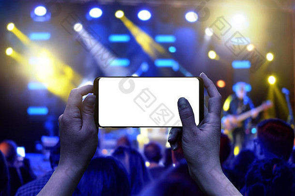手持带有独立显示屏的手机。水平位置。现场音乐会的背景。人群和灯光。