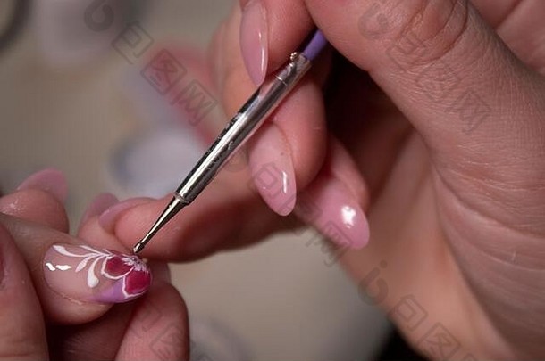 修指甲的过程。特写专业美甲师的手，在指甲上涂抹小石头。修指甲的概念。美的概念。虫胶凝胶上光剂