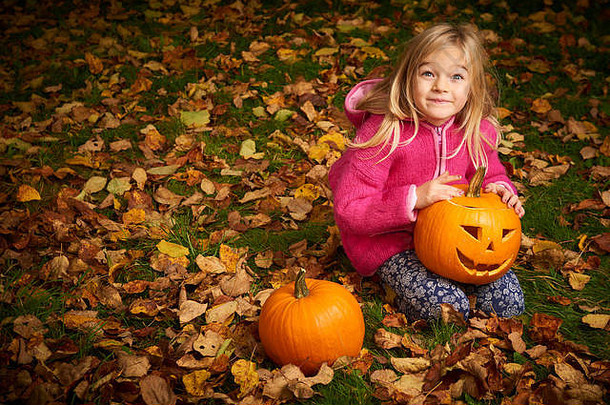 孩子可爱的金发碧眼的女孩玩秋天叶子万圣节南瓜