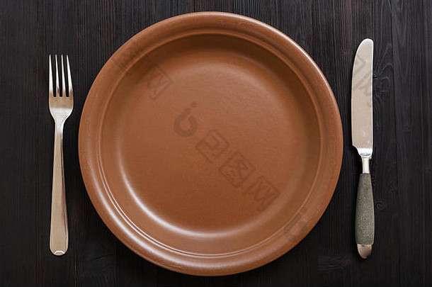 食物概念-深棕色桌子上带刀和勺子的棕色盘子的俯视图