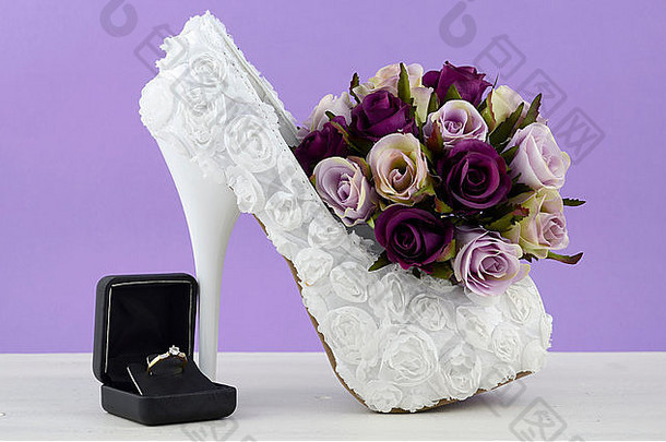 婚礼主题白色花朵新娘鞋，在破旧别致的白色桌子和紫色背景上有花朵。