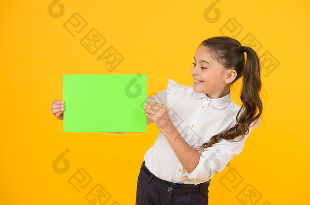 鲜艳的颜色。小女孩拿着黄色背景上的一张空纸。带着空白绿皮书完成作业或项目工作的小孩。<strong>试卷</strong>。复印纸，复印空间。