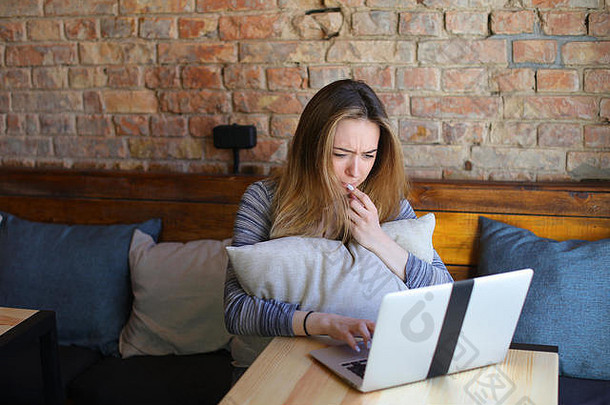 这位年轻女子坐在舒适的咖啡馆里，端着一杯卡布奇诺，用笔记本电脑聊天。