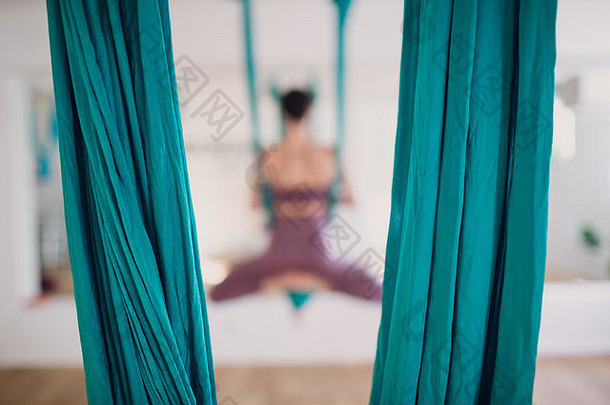 空中反重力瑜伽概念。使用绿色吊床在反重力瑜伽工作室练习飞行瑜伽的女士。