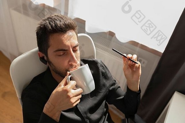 由于CVID2019冠状病毒疾病，一名男子在家工作。一个人在电脑前工作时喝咖啡。