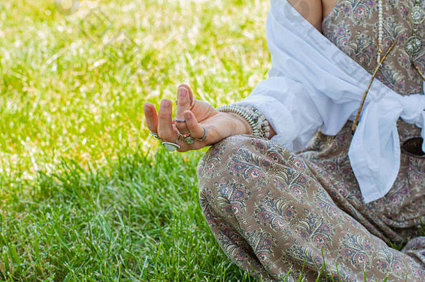 那个女人正坐在公园的草地上以莲花的姿势冥想。波西米亚风格，配饰、戒指和手镯，享受夏日时光。
