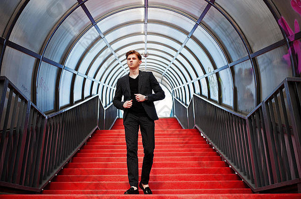 穿着黑色夹克的年轻时尚男子汉摆出街头户外的姿势。红楼梯上的惊人模特。