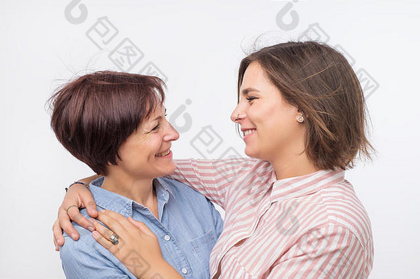 美丽的老妈妈和她成年的女儿拥抱在一起，看着相机，面带微笑。