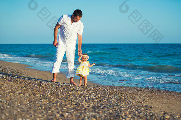幸福的家庭，爸爸带着女儿在沙滩上，学习走路。