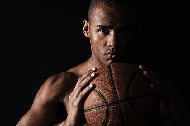 在黑色背景上，严肃的美国黑人篮球运动员双手拿着球，在相机前晃来晃去的特写镜头