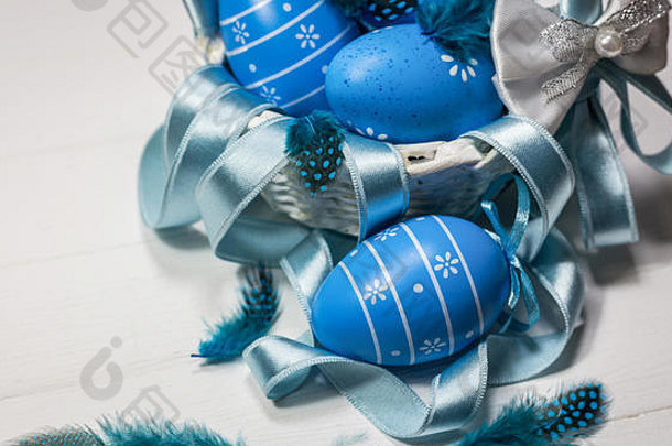 复活节的背景是蓝色的鸡蛋、羽毛和白色篮子里的缎带。具有空间的特写视图。
