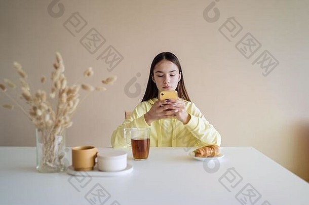 可爱的少女一边用智能手机一边在厨房吃早餐