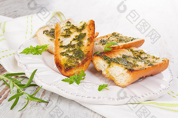 白色木质背景上的白色木制复古盘上有新鲜香草的大蒜法式面包。烹饪，复古乡村风格