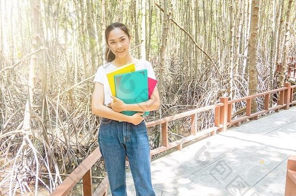 在红树林中，一个女孩胸前放着三本书，有<strong>漏光</strong>的效果。