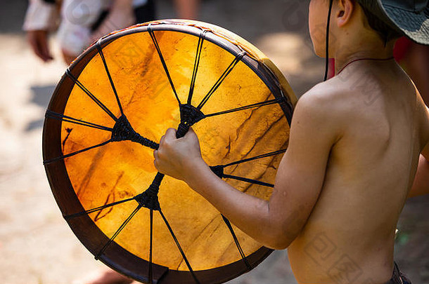 特写镜头：赤膊上阵的小孩在森林里的一次户外精神聚会上玩美洲土著人的神圣<strong>鼓</strong>
