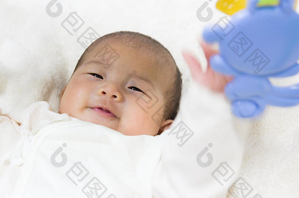 特写镜头：两个月大的新生亚洲可爱婴儿在玩健身玩具，白色床背景，精选焦点。