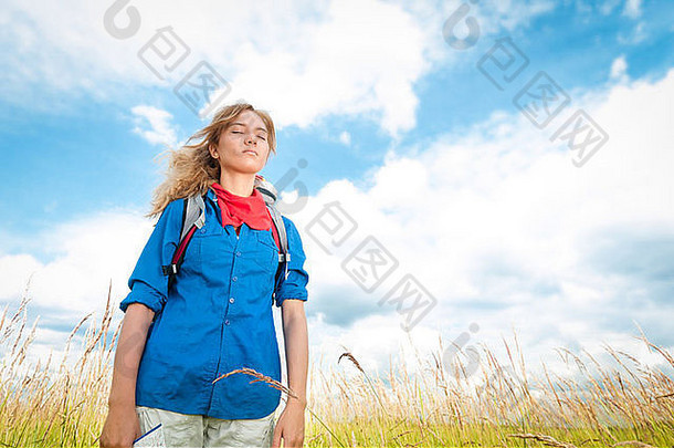 漂亮的年轻的旅游女人关闭眼睛享受新鲜的空气小麦场蓝色的多云的天空背景旅游旅行