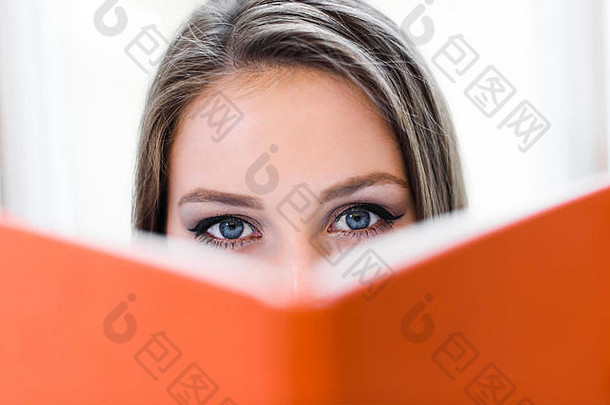 漂亮的金发女学生在橙色的书后面捂着脸。