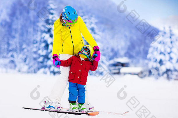 母亲和小孩在阿尔卑斯山滑雪。带安全帽、护目镜和杆子的活跃的妈妈和蹒跚学步的孩子。滑雪课