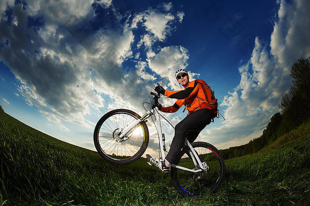 穿着橙色运动衫的骑自行车的人骑在绿色的夏季田野上