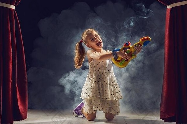 可爱的小女孩在舞台上弹吉他。这孩子梦想成为一名摇滚音乐家。