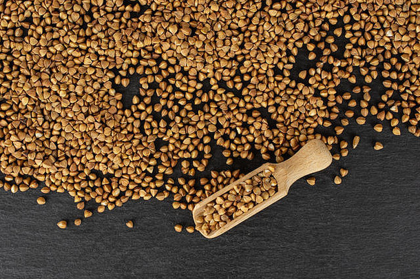 大量未经的棕色荞麦颗粒，木质勺平放在灰色石头上