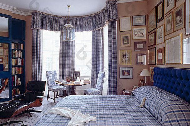 在传统的粉红色卧室里，蓝色格子床单和相配的窗帘，窗户里有桌子和椅子