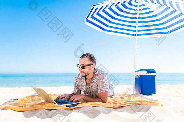 年轻的男人。移动PC工作沙子海滩