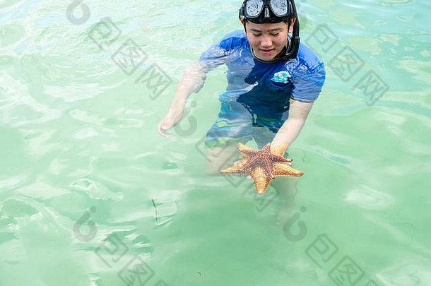 在大开曼岛附近的加勒比浅水区，一个男孩手里拿着两颗沉入水中的海星