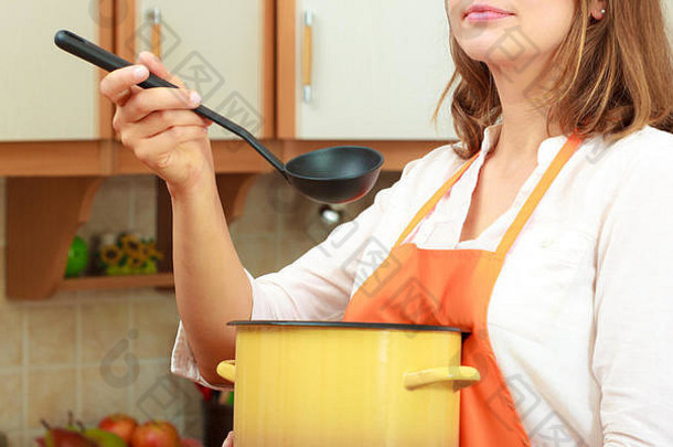 家庭主妇使汤餐晚餐中间岁的女人持有勺子包能管家穿橙色围裙准备食物