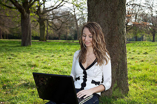 坐在公园里拿着笔记本电脑的女人