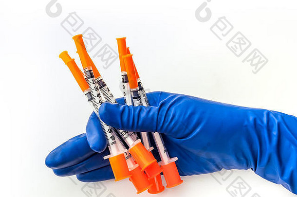 医生的手戴着蓝色医用手套，手里拿着几支注射器，医用溶液背景为白色。流感疫苗
