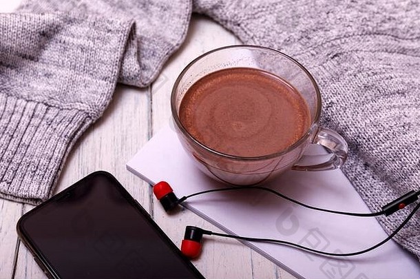 一杯热咖啡或热巧克力，带耳机，放在质朴的木桌上，特写照片，带马克杯的保暖毛衣，冬季早晨概念，俯视图