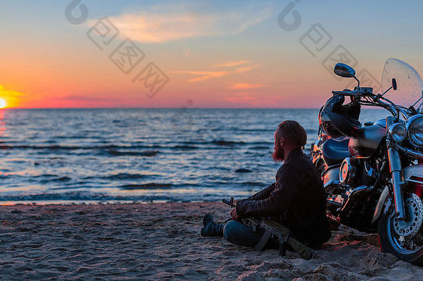 在日落的背景下，一个骑着摩托车的野蛮人在海边的沙滩上