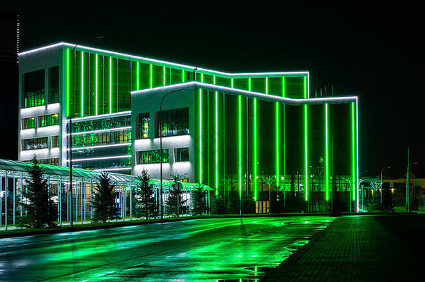 由一排绿色霓虹灯构成的现代科技大楼。夜市迷人的景色，霓虹灯反射在潮湿的道路上。