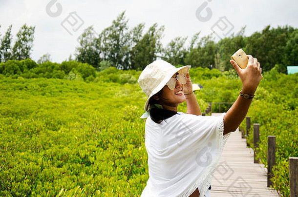旅行者泰国妇女使用智能手机在木桥上拍照旅行，参观金色红树林，泰国名东邦通森林，当地巴基斯坦