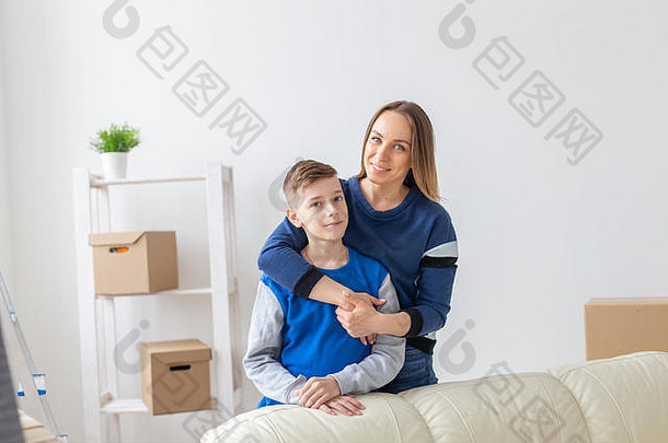 积极微笑的母亲和迷人的儿子正站在一间明亮舒适的新公寓里摆姿势。新房的搬家和抵押的概念