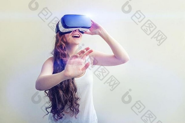 在白色背景下，戴着虚拟现实VR眼镜和头盔耳机的年轻女子微笑。智能手机使用虚拟现实护目镜。技术、模拟、高科技、电子游戏概念