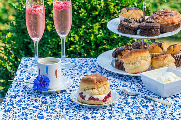 下午茶，<strong>蛋糕</strong>和传统的英国烤饼，草莓酱和凝块奶油摆在花园的桌子上。户外用餐。