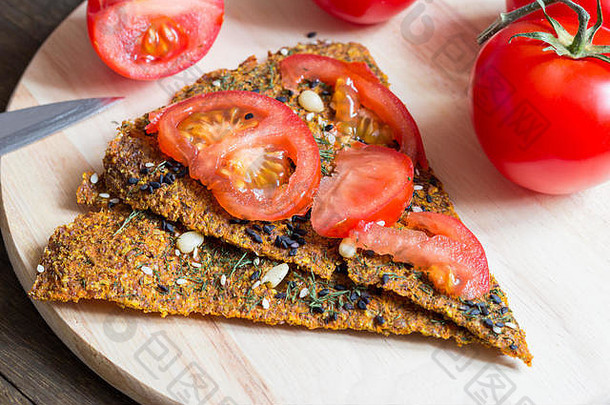 生的纯素面包，上面有西红柿片，放在深色木桌上的厨房板上。简单的健康膳食三明治。健康膳食概念。