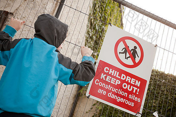 一个小男孩爬上有警告标志的篱笆