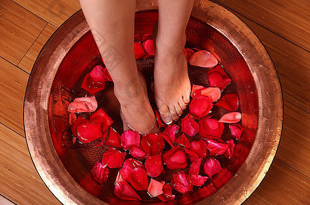 女人的脚在装满水和玫瑰叶的盆里