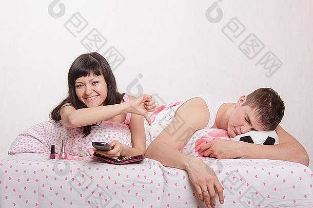 一个年轻的女孩和一个躺在床上的男人。那个漂亮的女孩手上修了指甲，那个在电视上看足球的家伙