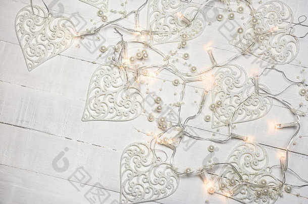 白色木质背景上的圣诞假期构图，心形装饰物和珍珠装饰灯。具有空间的俯视图。