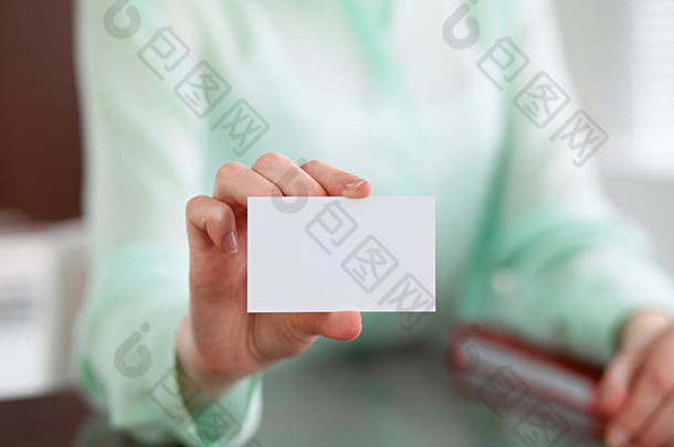 一位女商人递上一件绿色上衣，坐在办公室的办公桌旁，手里拿着名片。