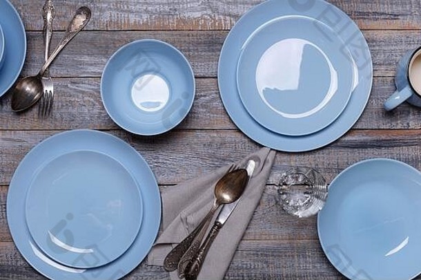 蓝色盘子、餐巾和餐具，背景是古老的灰色木质。从上面看。