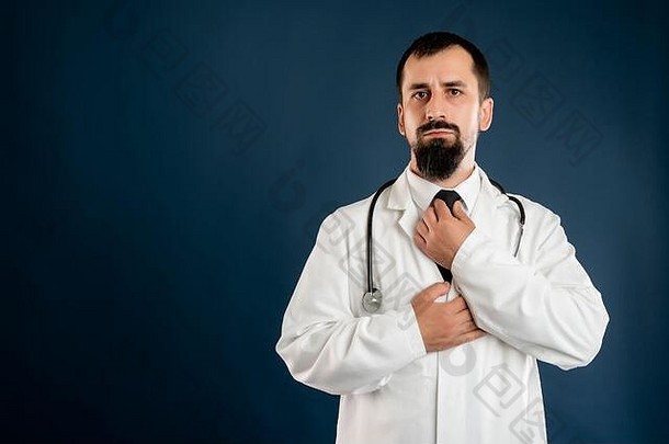 身着医疗制服、手持听诊器的男医生的肖像在蓝色隔离背景上摆出领带的姿势。